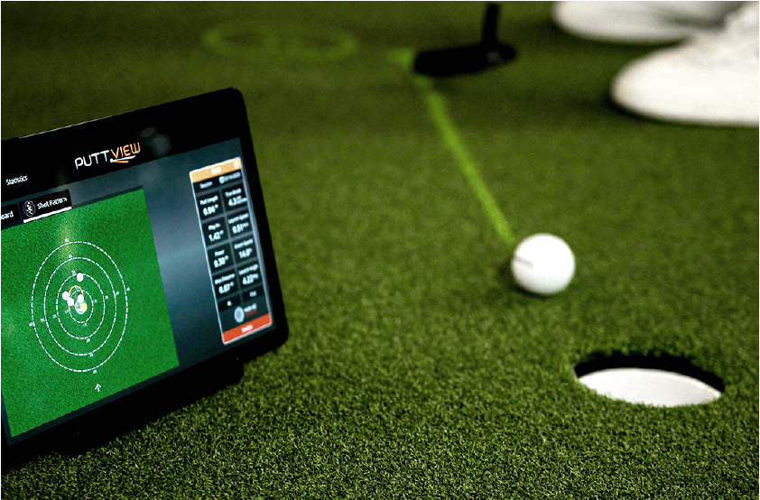 iPad on putting green next to a golf ball mid putt.